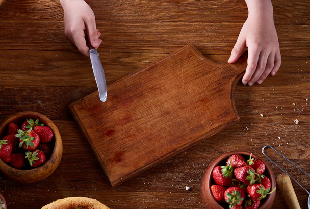 Knife in girls hand cutting a fresh strawberry on wooden table, top view, selctive focus. - Fotoğraf, Görsel