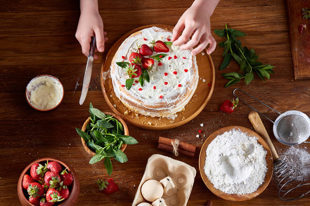 Top view of girls hands putting strawberries on cake, close-up, selctive focus, vertical. - 写真・画像