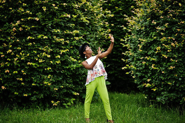 Amazing african american model woman in green pants and black hat posed at park. - Foto, afbeelding