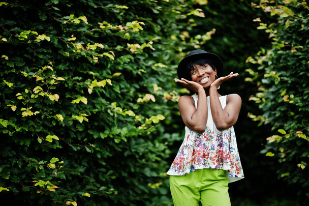 Amazing african american model woman in green pants and black hat posed at park. - Fotografie, Obrázek
