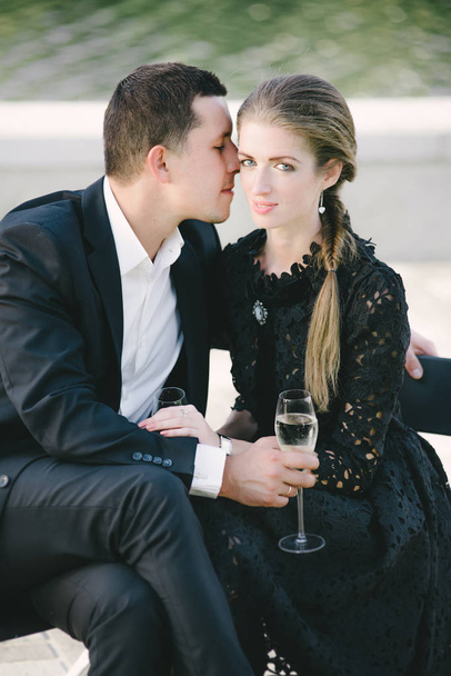 Young couple sitting close, man kissing her cheek, she looks confident, they are holding nice glasses - Foto, imagen