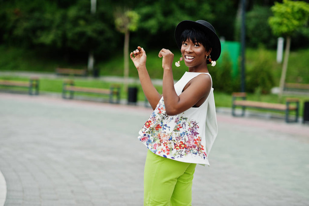 Amazing african american model woman in green pants and black hat posed at park. - Zdjęcie, obraz
