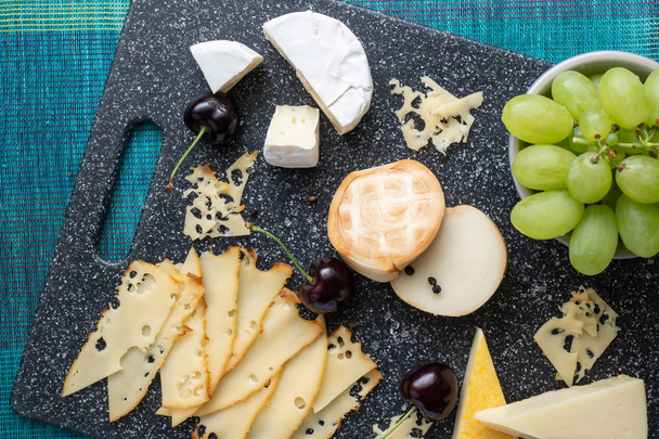 Cold appetizer. Cold cuts. Cheese on cutting board isolated on blue background, top view - Foto, afbeelding