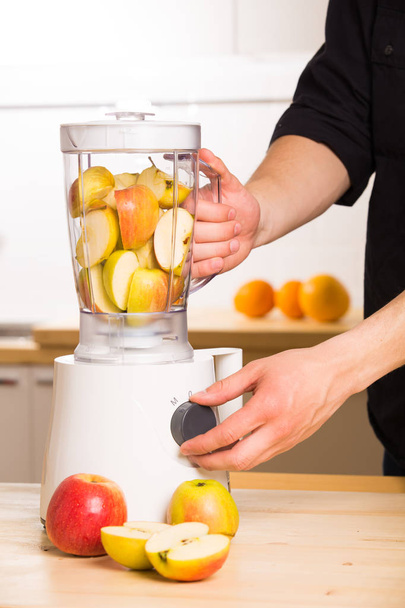 Young man cooking apple smoothie in blender - Foto, afbeelding