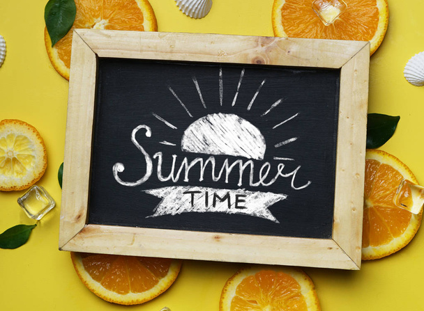 Tipografía de la hora de verano en pizarra entre accesorios de playa de verano sobre fondo amarillo
 - Foto, Imagen