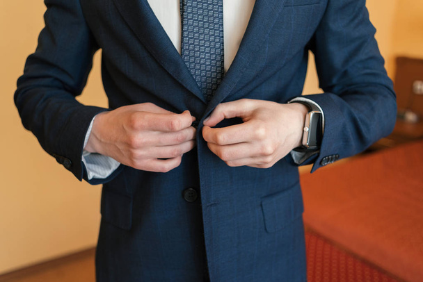 The groom fastens the button on his jacket - 写真・画像