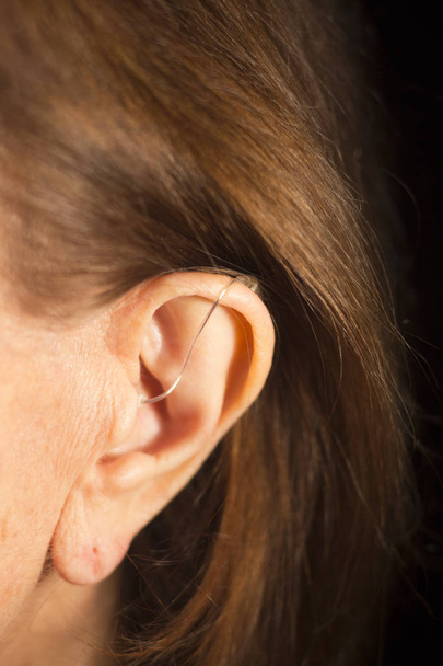 Głucha starsza pani nosząca nowoczesny cyfrowy aparat słuchowy w uchu. - Zdjęcie, obraz