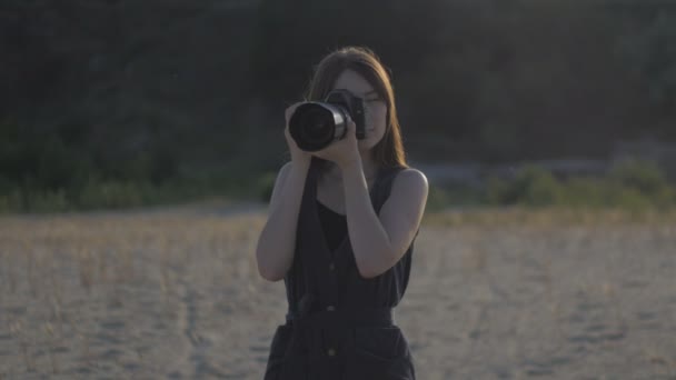 Jovem fotógrafo mulher bonita com o ourdoor câmera profissional. Menina está fazendo um tiro e olhando para a foto na câmera
 - Filmagem, Vídeo