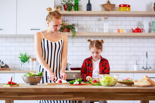 Photo of beautiful woman with her daughter cutting vegetables in kitchen - Foto, Bild