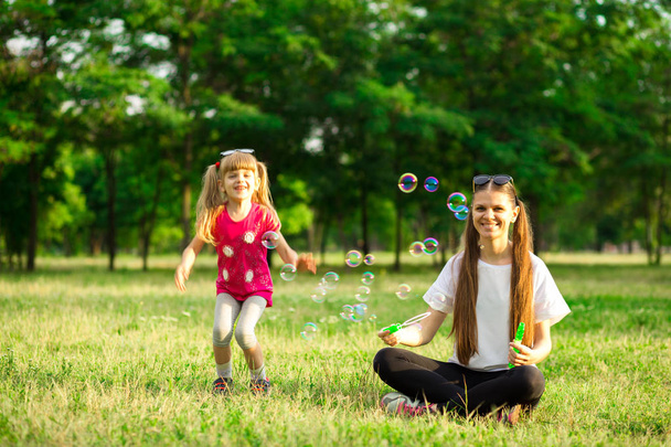 Madre joven e hija pequeña jugando en el parque con burbujas de jabón. Amor familia, paternidad, infancia
 - Foto, imagen