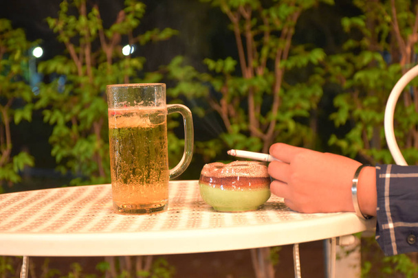 ein Glas kühles Bier auf dem Tisch, neben einem Glas liegt eine Hand  - Foto, Bild