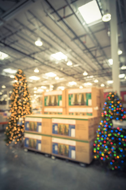 Vintage θολή εικόνα τεράστιο χριστουγεννιάτικο δέντρο διακόσμηση στο κατάστημα χονδρικής πώλησης. Στεφάνια και συμβολοσειρές bokeh φωτός περιβάλλουν το τεχνητό χριστουγεννιάτικο δέντρο. Χριστουγεννιάτικα διακοσμητικά παιχνίδια προς πώληση στην Αμερική - Φωτογραφία, εικόνα
