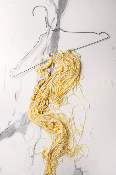 Homemade italian uncooked pasta spaghetti dried on clothes hanger over white marble texture background. Flat lay, space. - Fotografie, Obrázek