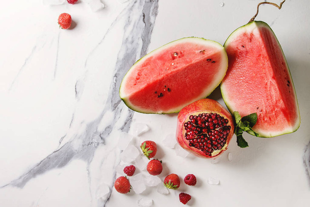 Variety of red ripe organic fruit berry watermelon, strawberry, raspberry, pomegranate for cocktails or smoothies with mint and crushed ice over white marble background. Flat lay - 写真・画像