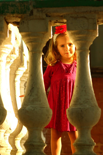 Sunlit retrato de uma menina bonito por trás banisters varanda velha
 - Foto, Imagem