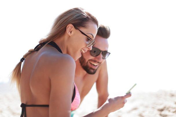 Smiling couple browsing their photos on the beach - 写真・画像