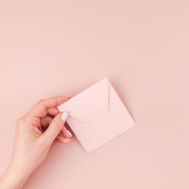 Creative image of woman hand holding small love letter with copy space on millennial pink background in minimalism style. Square Concept template for feminine blog, social media - Fotoğraf, Görsel