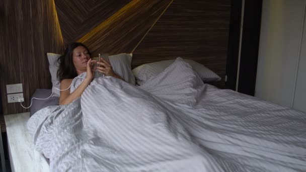 Una mujer se acuesta en la cama y disfruta del Smartphone
 - Imágenes, Vídeo