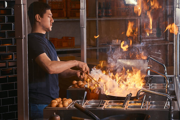 Cocinar es freír las verduras con especias y salsa en un wok en una llama. Proceso de cocción en un restaurante asiático
. - Foto, imagen