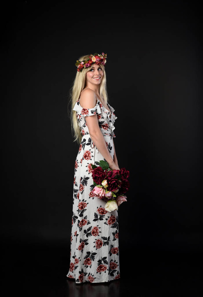 Ολόσωμο πορτρέτο του ξανθιά κοπέλα φορώντας floral φόρεμα και ένα στέμμα λουλούδι. όρθια στάση με φόντο μαύρο στούντιο. - Φωτογραφία, εικόνα