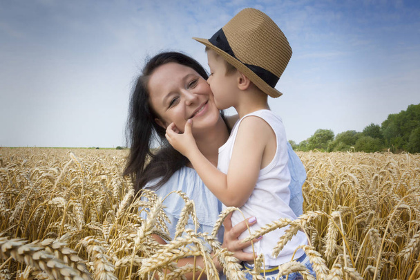 Happy family. Mom and son are laughing and talking on the wheat field. Front view. - 写真・画像