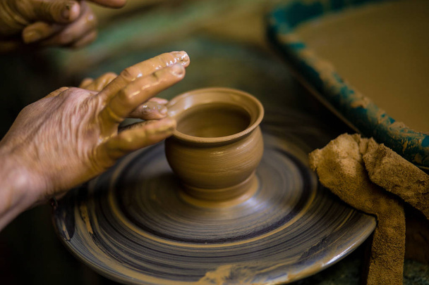 Close-up hands of potter in apron making vase from clay, selective focus. Making it together. Top view of potter teaching to make ceramic pot on pottery wheel - Photo, Image