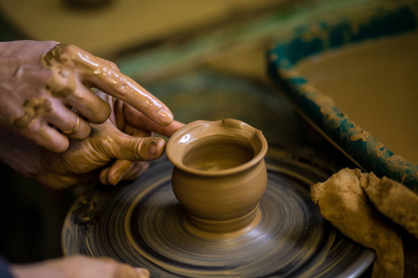 Close-up hands of potter in apron making vase from clay, selective focus. Making it together. Top view of potter teaching to make ceramic pot on pottery wheel - Foto, immagini
