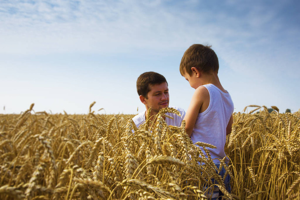Happy family. Father and son on the wheat field. Male shows the boy ear of wheat. - Fotografie, Obrázek