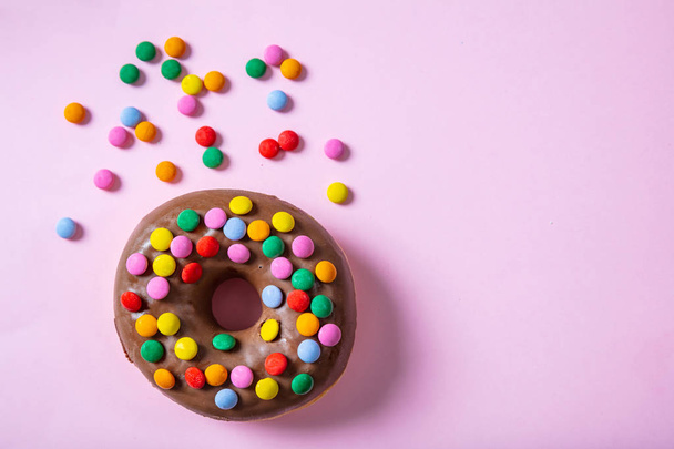 Concepto de pasteles. Donut con esmalte de chocolate con aspersiones, vista superior y aislado con espacio de copia sobre fondo rosa
. - Foto, Imagen