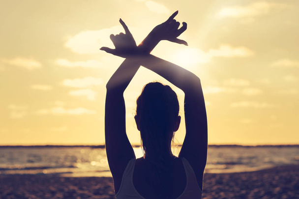 jonge vrouw silhouet beoefenen van yoga op het strand bij zonsondergang - Foto, afbeelding