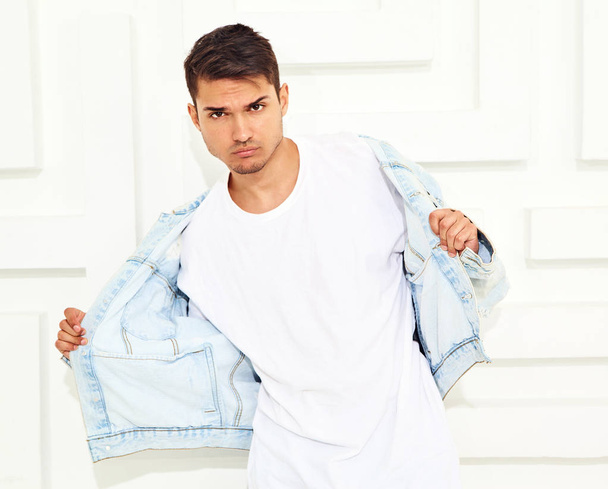 Portrait of handsome young model man dressed in jeans clothes posing near white textured wall - Foto, immagini