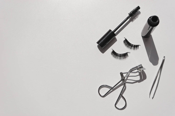 Black false lashes strips, mascara, tweezers, curler on white  - Φωτογραφία, εικόνα