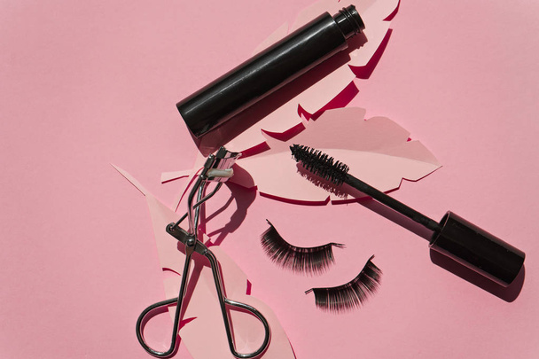 Zwarte valse wimpers strips, mascara, krultang op roze achtergrond  - Foto, afbeelding