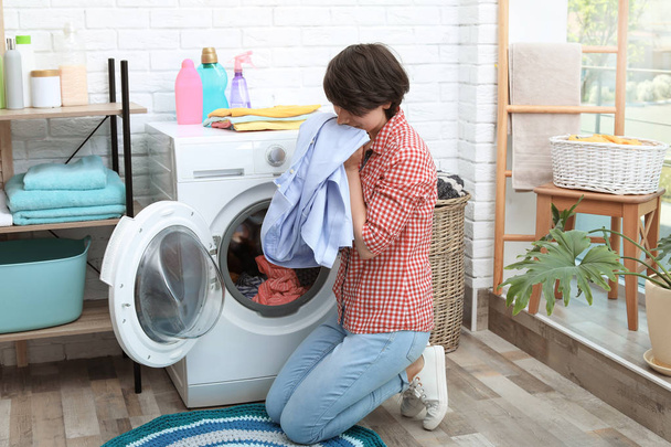 Young woman getting out clean clothes from washing machine at home - Foto, Bild