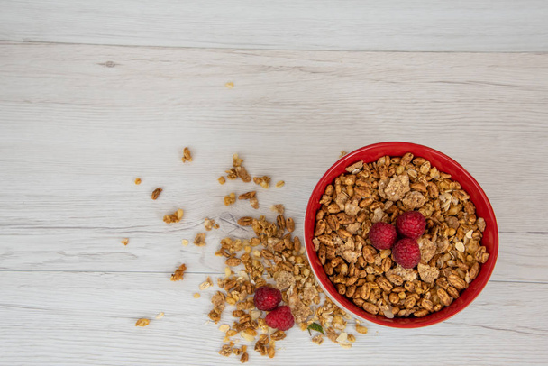 A red bowl on full of granola with berries on white wood table, top view,copy space - Foto, afbeelding