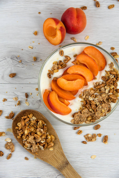 A bowl filled with apricot yoghurt and a wooden spoon full of granola on a white wood table, top view, copy space - Foto, Imagem