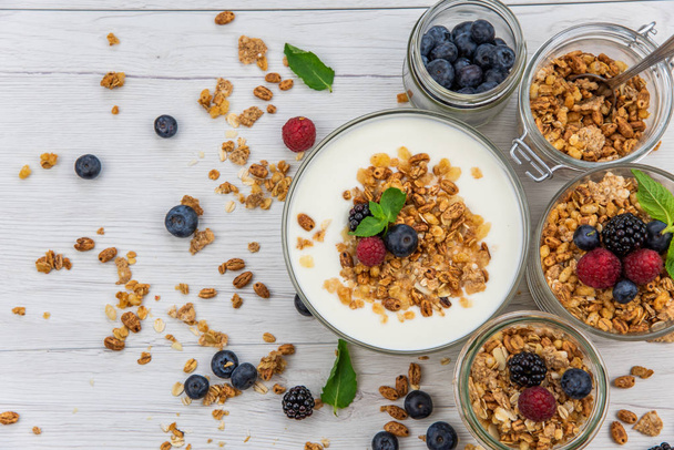 Jars full with granola, yogurt and fresh berries, top view, selective focus - Zdjęcie, obraz