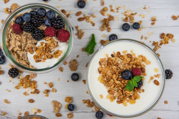 Bowsl of yogurt with granola and fresh berries on white wood table, top view - Foto, immagini