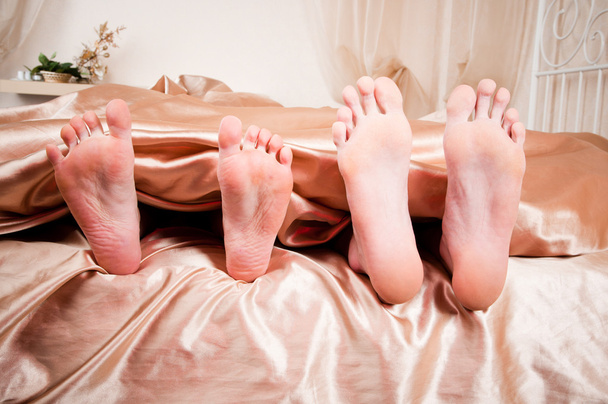 The bared heels of pair in stick out from under bed-sheets - Foto, Bild