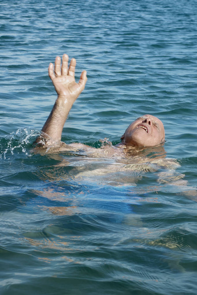 Vanha mies merellä hukkuu aivohalvauksen vuoksi ja pyytää apua kämmen ylöspäin
 - Valokuva, kuva