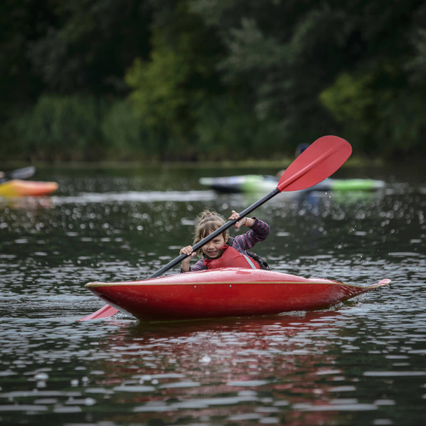young teenager girl actively manages a sports kayak boat on a beautiful river - 写真・画像