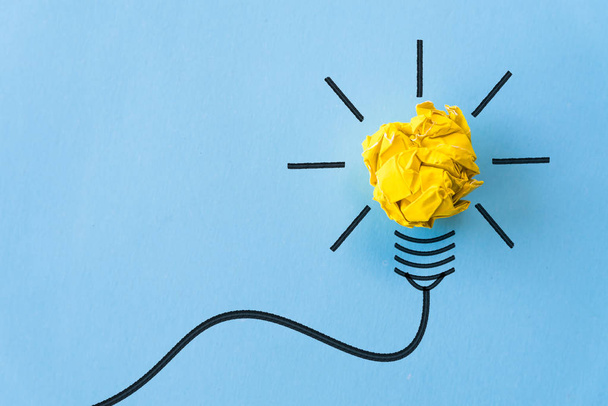 Inspiration und tolles Ideenkonzept. Glühbirne mit zerknittertem gelben Papier auf blauem Hintergrund. - Foto, Bild