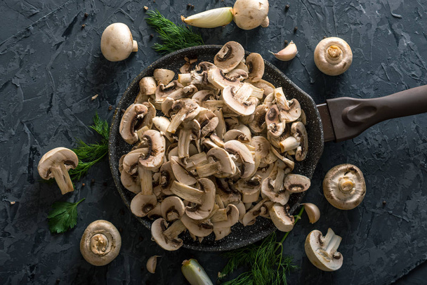 Champignons blancs frais tranchés dans une casserole sur la table de cuisine sombre. Le concept de la cuisson des plats de champignons. Gros plan
 - Photo, image