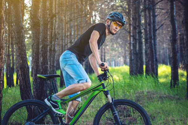 Un uomo in casco in sella ad una mountain bike verde nel bosco tra gli alberi. Ciclista in movimento. Concetto di stile di vita attivo e sano
 - Foto, immagini
