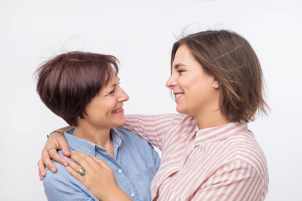 Beautiful maturesenior mom and her adult daughter are hugging, looking at camera and smiling. - Fotografie, Obrázek