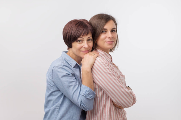 Beautiful maturesenior mom and her adult daughter are hugging, looking at camera and smiling. - Foto, Imagem