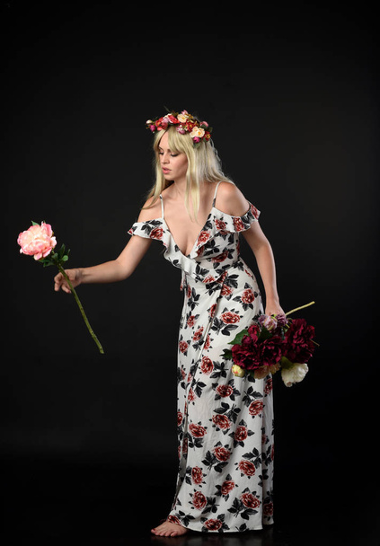 full length portrait of blonde girl wearing floral dress and a flower crown. standing pose against a black studio background. - Fotografie, Obrázek