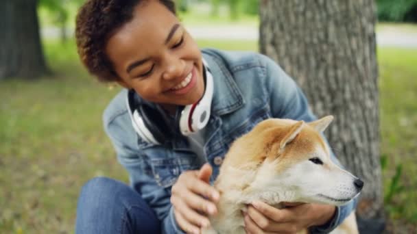 Slow motion of loving African American girl pet owner stroking its dog fussing fur on its neck and looking at animal with love and care. People and nature concept. - Imágenes, Vídeo