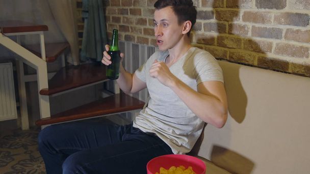Człowiek pije piwo i chipsy przed Tv oglądanie piłki nożnej. - Zdjęcie, obraz