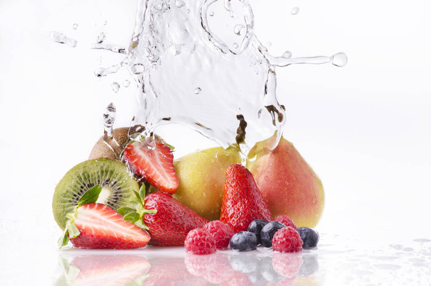 a wave of clear water falling on the varied and colorful fruits on a white background - Photo, Image